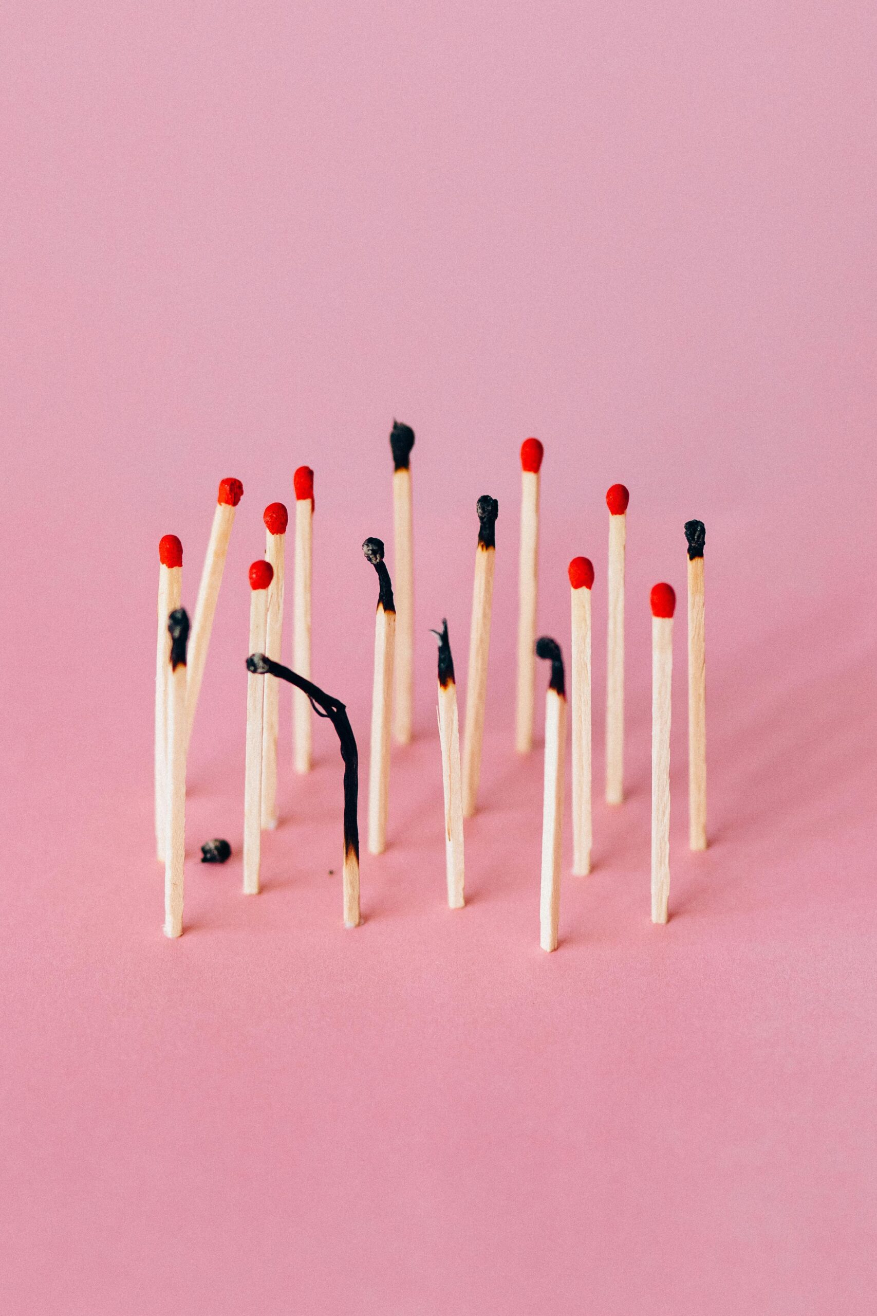 Artistic photo of burned matchsticks on pink background symbolizing burnout.