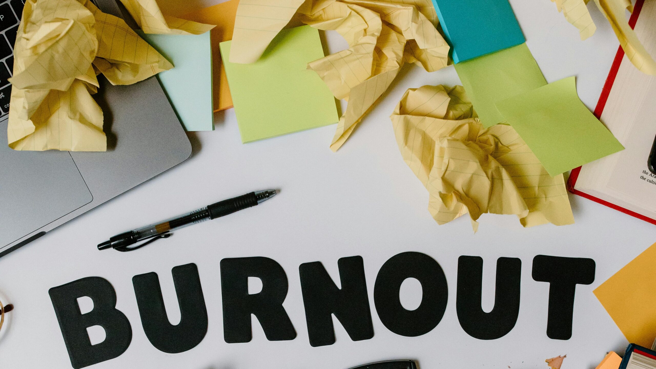 Symbolic image of burnout with crumpled papers and office supplies on a cluttered workspace.