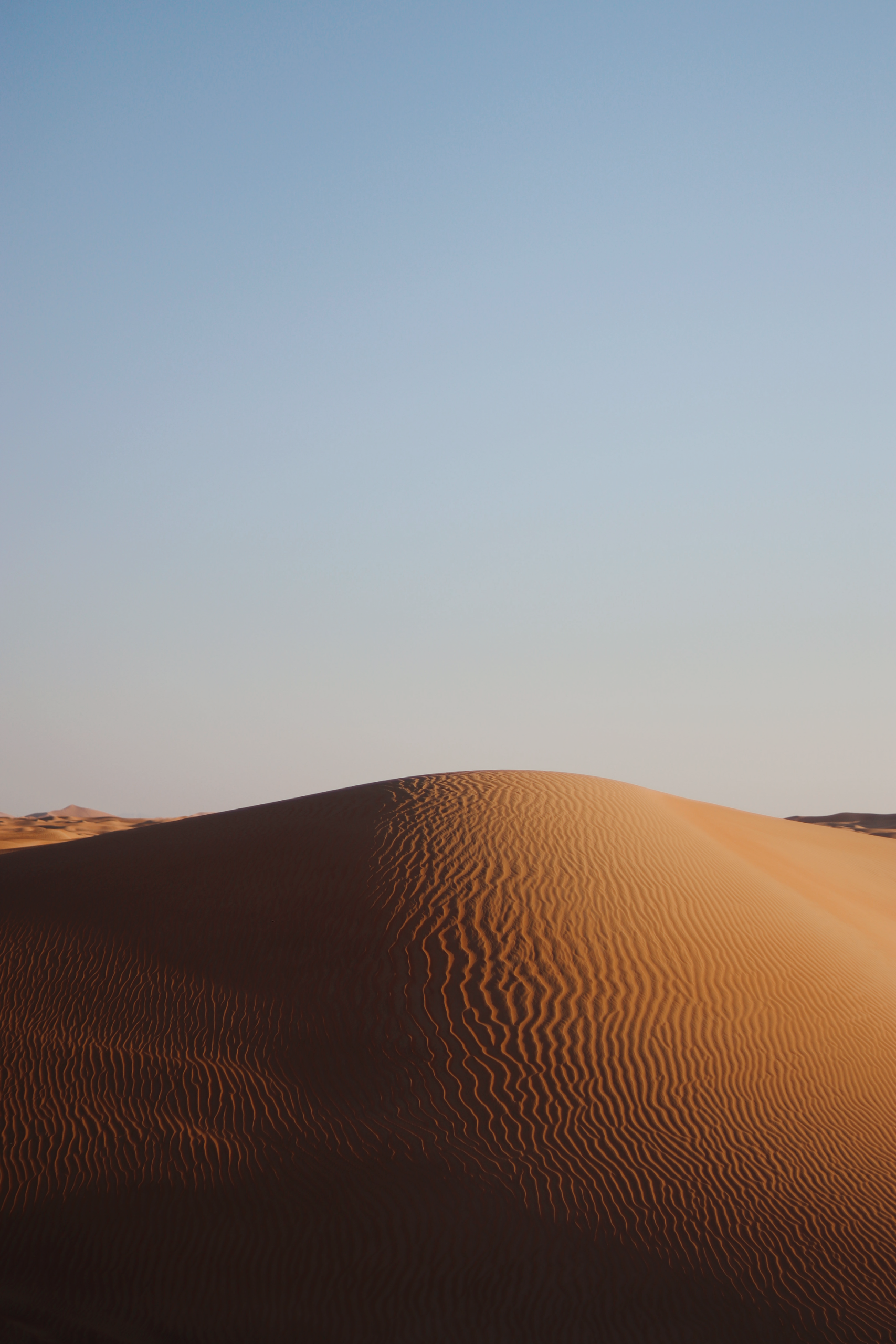Captivating view of a sunlit sand dune with clear blue sky background, showcasing natural desert beauty.