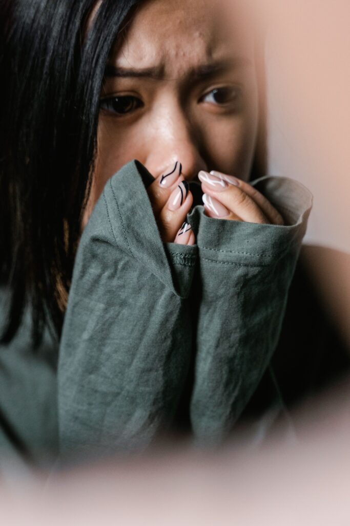 Crise d'angoisse. A woman appears anxious, covering her mouth with a green sweater sleeve in a close-up shot. 